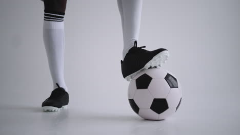 Close-up-of-the-foot-of-a-professional-black-football-player-standing-on-the-ball-in-slow-motion-in-the-white-background.-Brazilian-football-player-foot-on-the-ball-to-pose